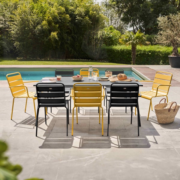 Moderner Garten-Essbereich mit dunklem rechteckigem Tisch und gelben sowie schwarzen Metallstühlen auf einer Steinterrasse am Pool.