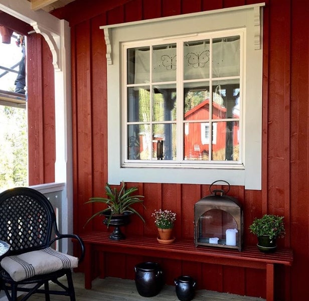 Holzveranda mit roter Fassade, Sprossenfenster, Sitzbank aus Holz und dekorativen Pflanzen in Töpfen.