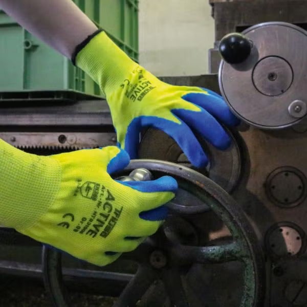 Person trägt Montagehandschuhe bei der Arbeit an einer Maschine.