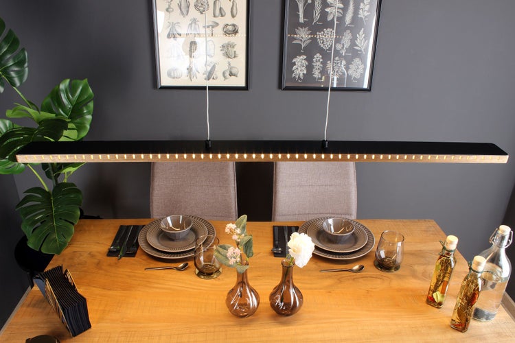 Moderne schwarze LED-Pendelleuchte über einem gedeckten Holzesstisch für zwei Personen, mit botanischen Wandbildern und einer Zimmerpflanze.