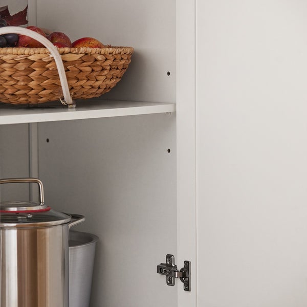 Innenansicht eines weißen Küchenschranks mit Regalen, Kochtopf und einem Korb mit Früchten.