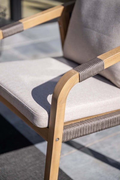 Detailansicht eines Gartenstuhls aus Holz mit grauer Seilumwicklung an den Armlehnen und hellen Sitzkissen.