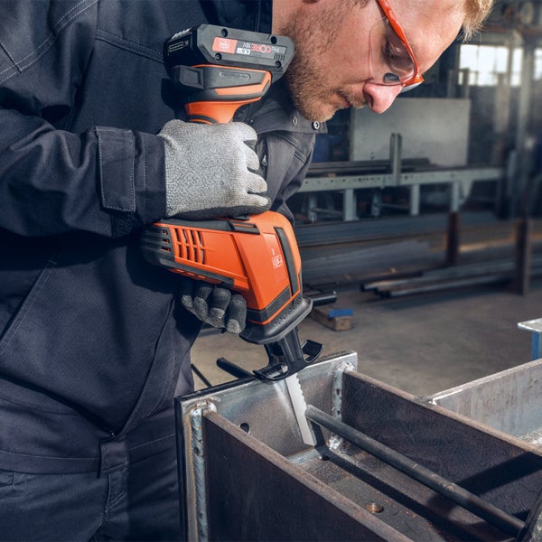 Handwerker schneidet mit einer Akku-Säbelsäge ein Metallprofil in einer Werkstatt. Er trägt Schutzhandschuhe und eine Sicherheitsbrille.