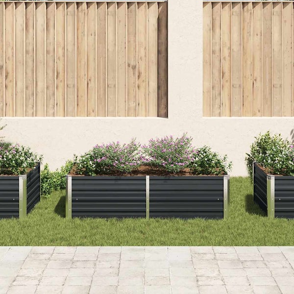 Hochbeet aus anthrazitfarbenem Metall mit silbernen Ecken, bepflanzt mit Blumen auf einem Rasen vor einer modernen Sichtschutzwand aus Holz.