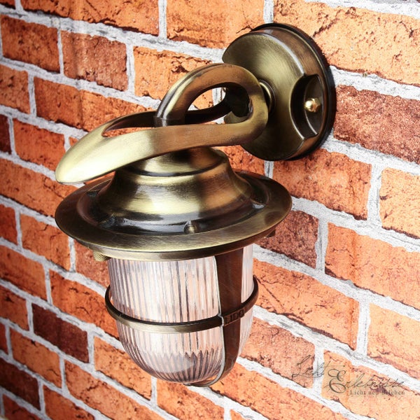 Messingfarbene Wandleuchte mit geriffeltem Lampenschirm an einer Backsteinmauer