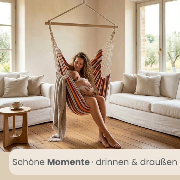 Gestreifter Hängesessel aus Stoff mit Holzstab in einem hellen Wohnzimmer mit weißen Sofas und Holzfußboden.