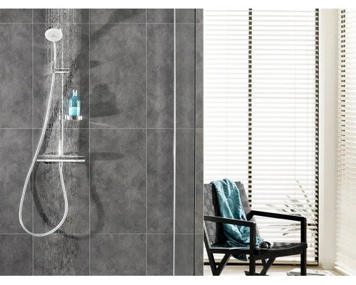 Moderne Dusche mit Duschstange, Armatur und Ablage in einem gefliesten Badezimmer mit Blick auf einen Sessel vor einem Fenster mit Jalousien.