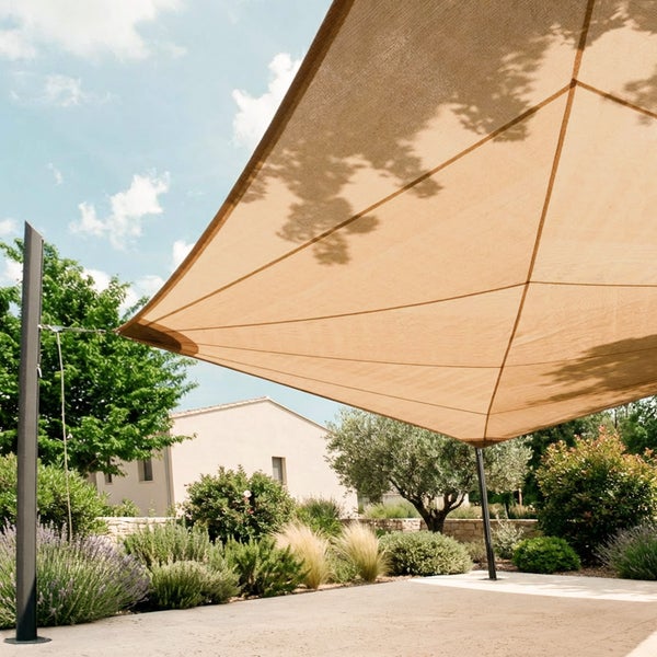 Großes Sonnensegel aus wetterfestem Gewebe über einer Terrasse, befestigt an Pfosten, umgeben von Gräsern, Lavendel und einem Haus im Hintergrund.