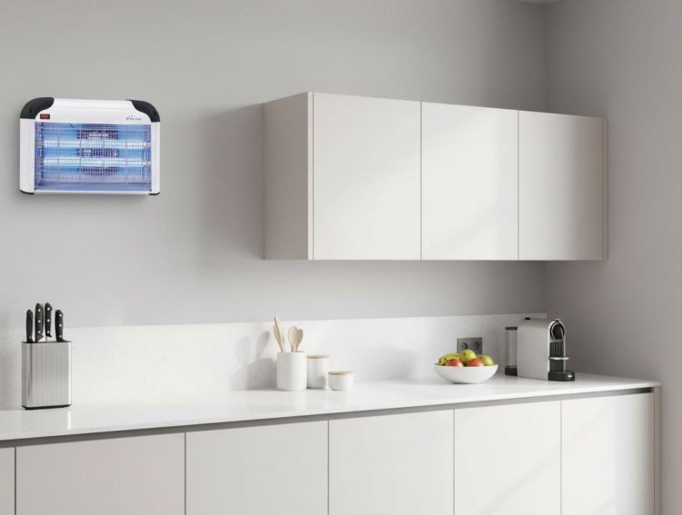 Elektrischer Insektenvernichter mit UV-Licht, an der Wand einer hellen, modernen Küche mit weißen Schränken montiert.