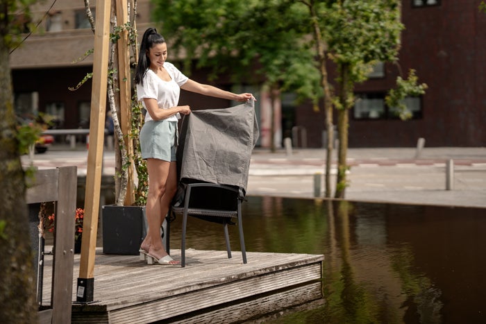 Frau deckt Gartenstuhl mit einer Schutzhülle ab