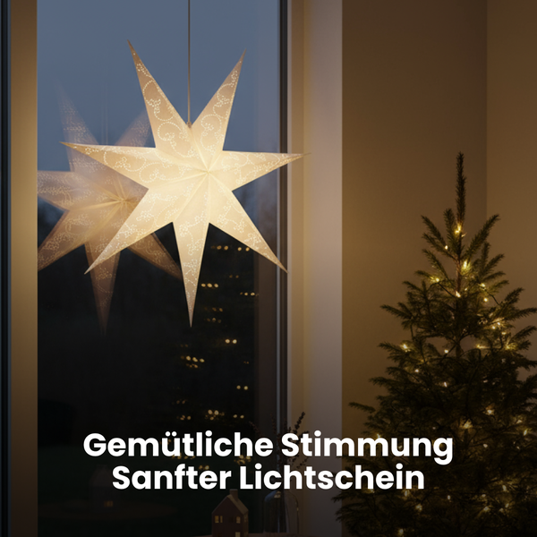 Dekorativer Papierstern am Fenster neben einem kleinen Weihnachtsbaum mit Lichtern