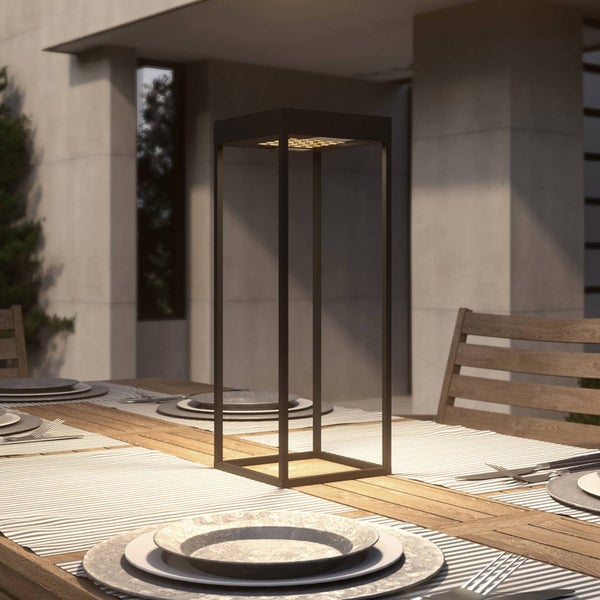 Moderne rechteckige Tischleuchte in minimalistischem Design auf einem gedeckten Holztisch im Außenbereich mit Betonwänden.