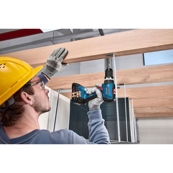 Ein Handwerker mit Schutzhelm und Schutzbrille benutzt einen Akkuschrauber, um Holzbalken zu befestigen.