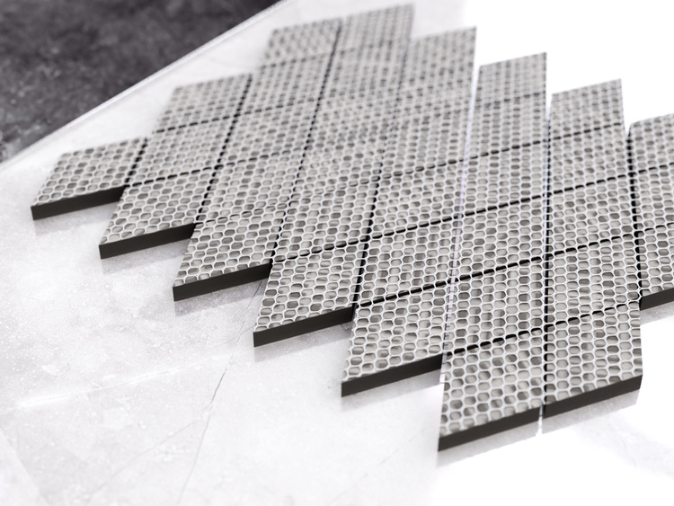 Nahaufnahme einer Mosaikfliesenmatte mit kreisförmigem Lochmuster, graue Fliesen mit schwarzer Rückseite.