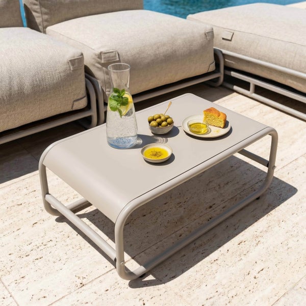 Moderner rechteckiger Outdoor-Couchtisch mit abgerundetem Rohrgestell auf einer Steinterrasse neben einem Loungesofa.
