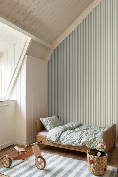 Helles, organisiertes Kinderzimmer im modernen Stil mit vertikal gestreifter Vliestapete, Holzbett, gestreifter Bettwäsche, Holzspielzeug und gestreiftem Teppich unter einer Dachschräge.