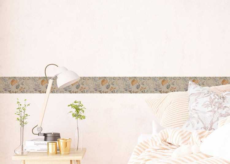 Tapetenbordüre mit botanischem Blätter- und Blumenmuster an der Wand in einem hellen Schlafzimmer mit Nachttisch und Lampe.