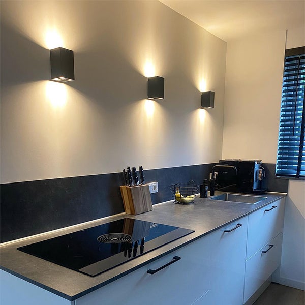 Moderne Küche mit schwarzen Wandleuchten, Kochfeld, Spüle und Küchenutensilien.