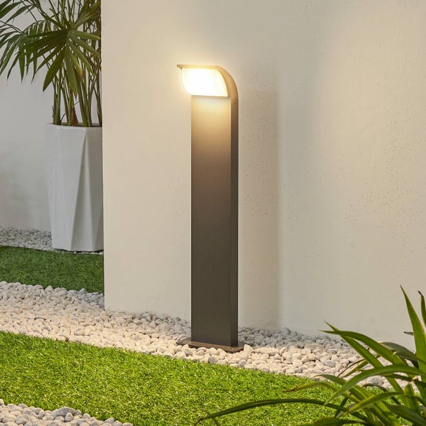 Moderne LED-Wegelampe in Anthrazit auf weißen Kieseln neben einer Rasenfläche und einer weißen Wand.