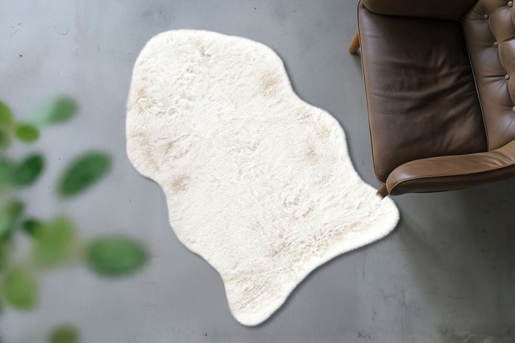 Ein hochwertiges Fellimitat Schaffell als Wohnzimmerteppich in organischer Form auf einem Boden neben einem Ledersessel.