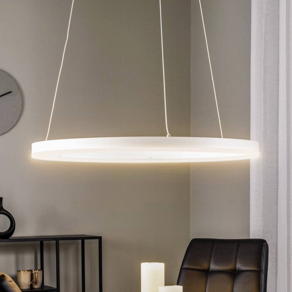 Moderne ringförmige LED-Pendelleuchte in einem hellen Wohnraum mit Stuhl und Regal.