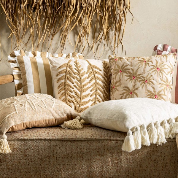 Dekorative Kissen mit verschiedenen Motiven und Texturen auf einem Sofa.