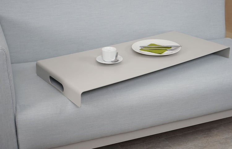 Modernes, minimalistisches Sofatablett mit Griffen auf einem Sofa, bestückt mit einer Kaffeetasse und einem Teller.
