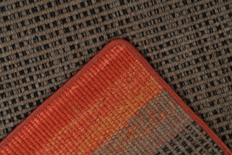 Gewebter Teppich mit orange-braun gestreifter Ecke und rotem Rand auf braun-schwarz kariertem Muster.