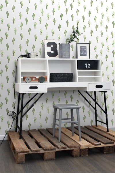 Szene mit Schreibtisch, Stuhl und Dekoration vor einer Wand mit Kaktusmuster