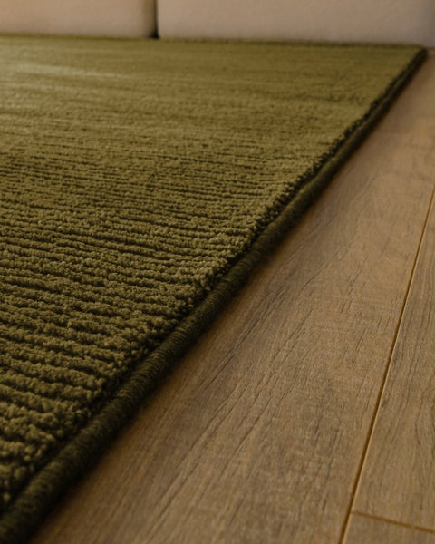 Strukturierter Teppich mit Rippenmuster in einem Wohnraum unter einem Hocker.