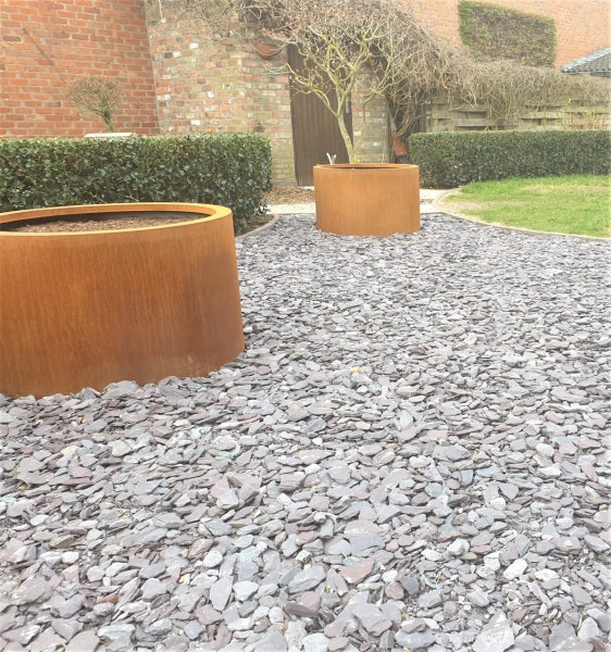 Moderner Garten mit zwei runden Pflanzkübeln aus Corten-Stahl auf einer Fläche aus Schiefer-Splitt.