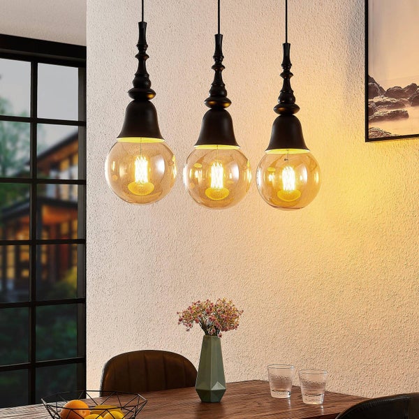 Drei Pendelleuchten mit Lampenschirmen aus Glas und Metallelementen über einem Esstisch.