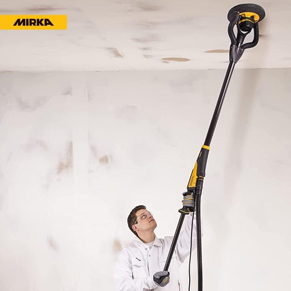 Ein Arbeiter verwendet einen Mirka Langhalsschleifer mit langem Griff, um eine Decke zu schleifen. Mirka Logo sichtbar.