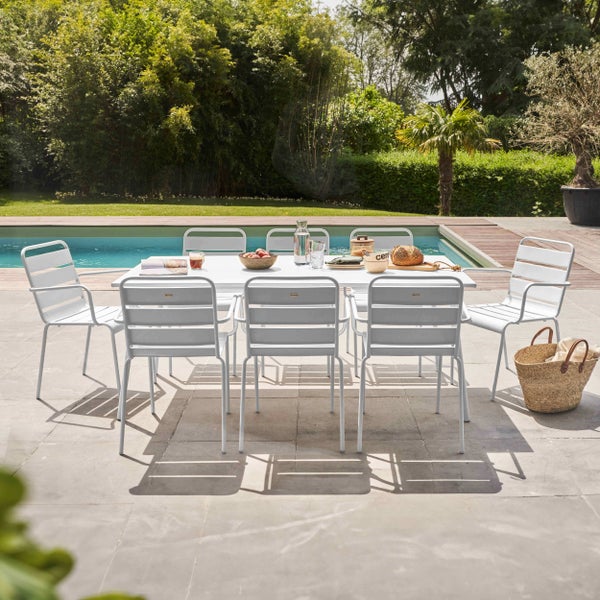 Modernes weißes Gartenmöbel-Set mit einem rechteckigen Tisch und acht Stühlen auf einer hellen Steinterrasse neben einem Pool im Garten.