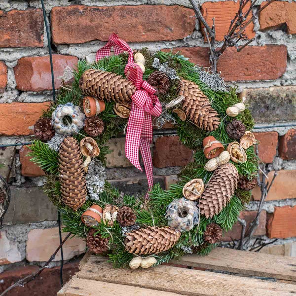 Dekorativer Adventskranz mit Tannenzapfen und karierter Schleife an einer Ziegelwand