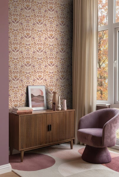 Wohnraum mit gemusterter Vliestapete mit Blumenmotiven, Sideboard aus Holz, gepolstertem Sessel und gemustertem Teppich.