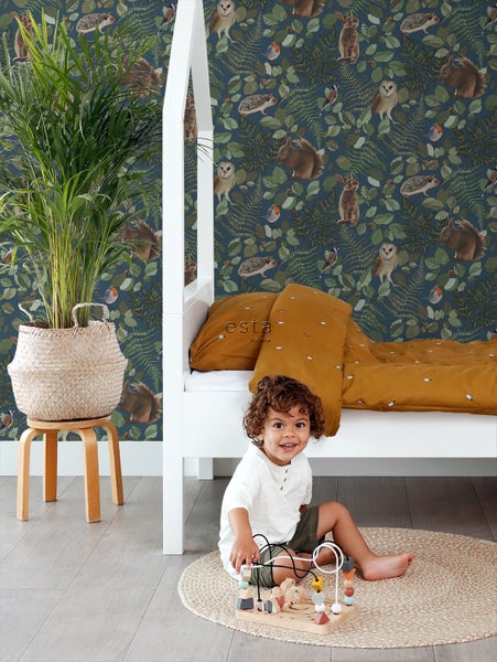 Kinderzimmer mit Bett, Pflanze und Kind auf einem Teppich vor einer Tapete mit Tiermotiven.