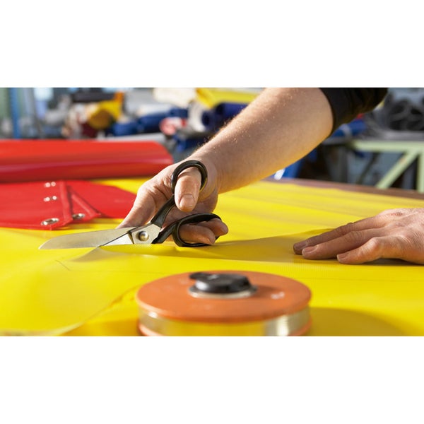 Zuschneiden einer gelben Plane mit einer Schere in einer Werkstatt.