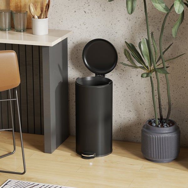 Schwarzer Tretabfalleimer aus Metall mit geöffnetem Deckel in einer modernen Küche neben einer Zimmerpflanze.