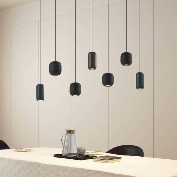 Moderne Pendelleuchten in verschiedenen Formen und Farben hängen in unterschiedlichen Höhen über einem gedeckten Esstisch vor einer hellen Wand.