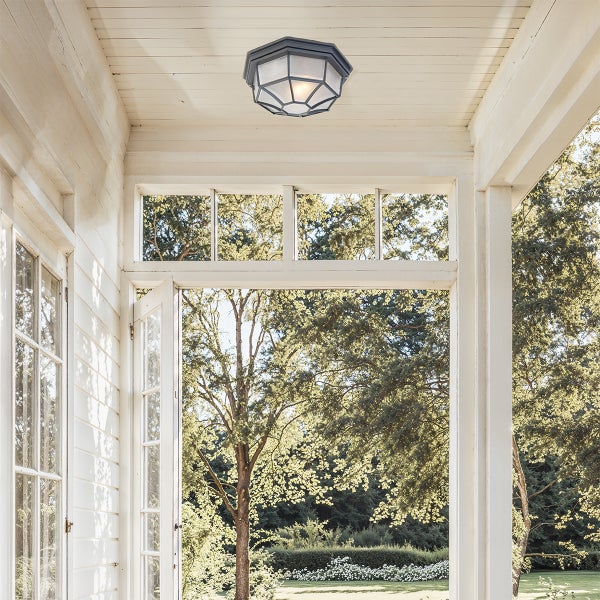 Sechseckige Außenleuchte an der Holzdecke einer hellen Veranda mit Ausblick in einen begrünten Garten.