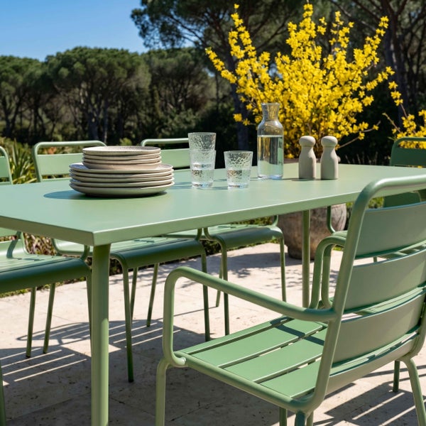 Grünes Gartenmöbel-Set aus Metall bestehend aus Tisch und Stühlen auf einer hellen Terrasse in einem Garten.