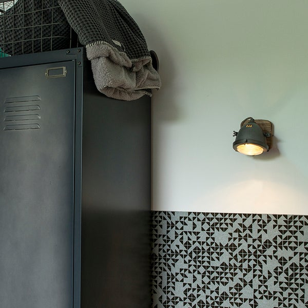 Szene mit einem grauen Metallschrank, einer Wandleuchte und gemusterten Fliesen.