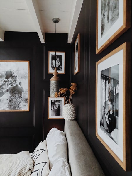 Schlafzimmerwand mit gerahmten Schwarz-Weiß-Fotografien, dekorativen Elementen und Kissen auf dem Bett