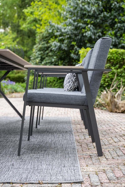 Modern gestalteter Außenbereich mit gepolsterten Gartenstühlen aus Metall und Holz, einem Gartentisch und einem Outdoorteppich.