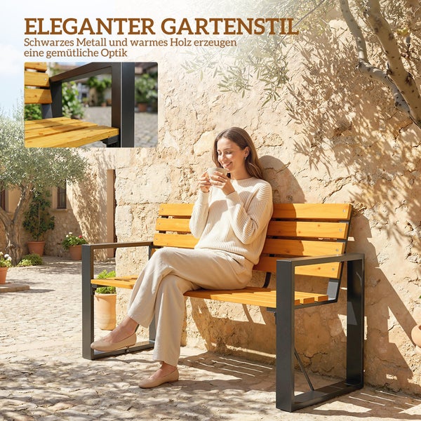 Moderne, elegante Gartenbank aus schwarzem Metall und hellem Holz vor einer Steinwand in einem hellen, sonnigen Garten.
