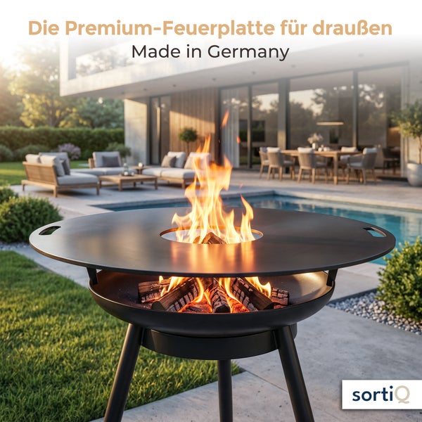 Eine runde Grill-Feuerplatte von SortiQ auf einer Terrasse mit brennendem Holzfeuer in einer modernen Außenanlage mit Pool.
