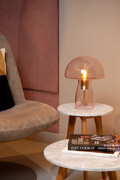 Dekorative Innenraumszene mit einer Pilzlampe auf einem Beistelltisch, einem Sessel und Kochbüchern.