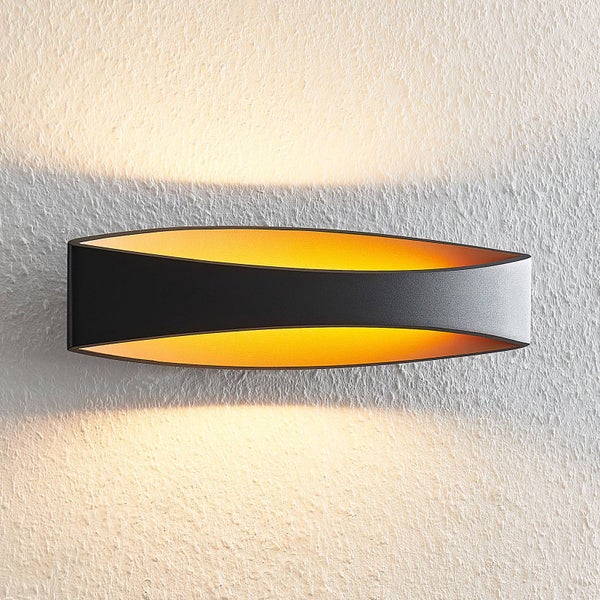 Moderne ovale Wandlampe in Schwarz mit goldener Innenseite, Lichtaustritt nach oben und unten an einer strukturierten Wand.