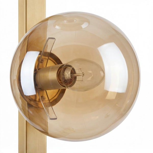 Nahaufnahme einer Wandleuchte mit kugelförmigem Glasschirm in Bernsteinoptik und goldfarbenem Metallgestell inklusive Leuchtmittel.